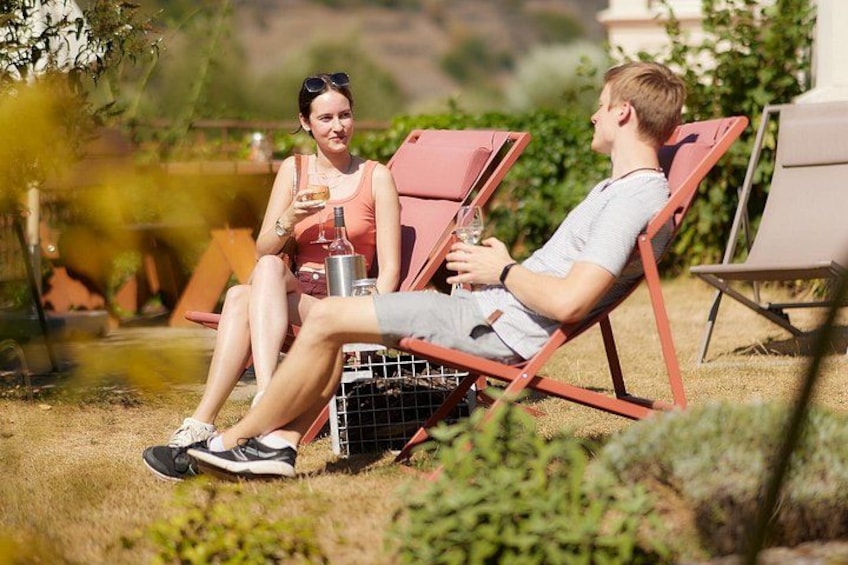 Due persone sedute su sedie rosse da giardino all'aperto, una delle quali tiene in mano una bevanda. 2