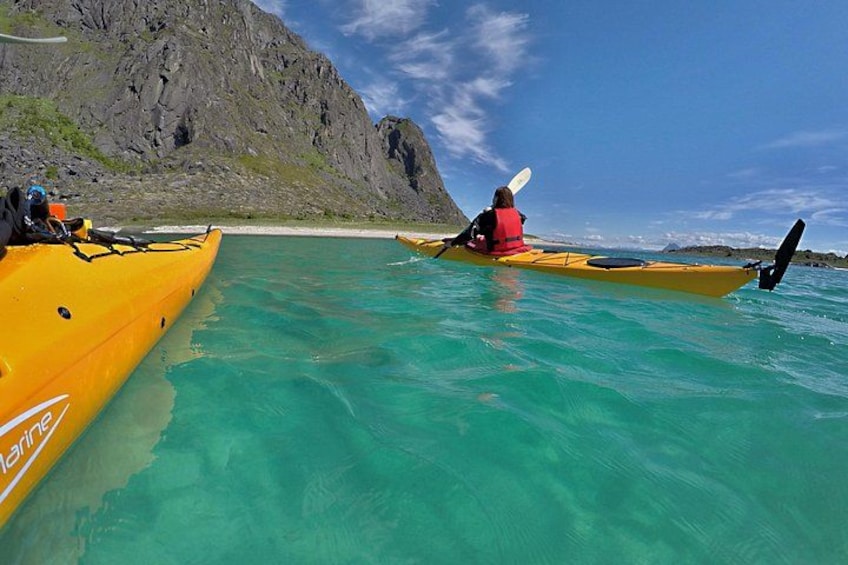 Un kayakiste dans un kayak jaune, sur une eau turquoise et limpide, avec une côte rocheuse en arrière-plan. 1