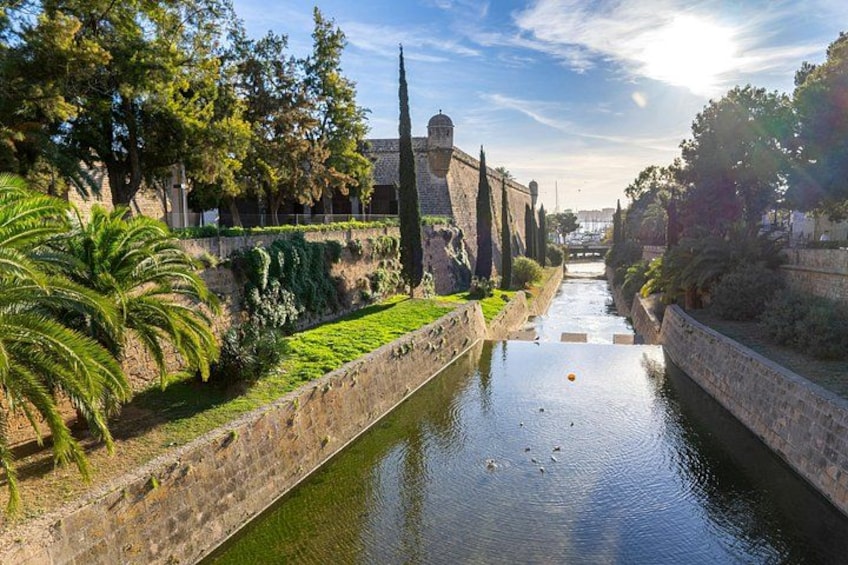 A canal flanked by stone walls and greenery, with a tower in the background. 2