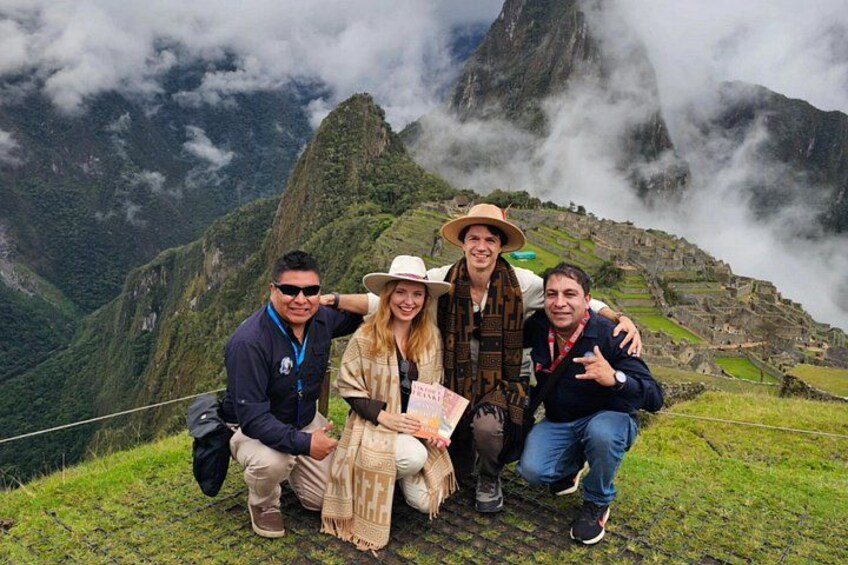 Un grupo de personas posando en una colina cubierta de hierba, con un paisaje montañoso al fondo. 2