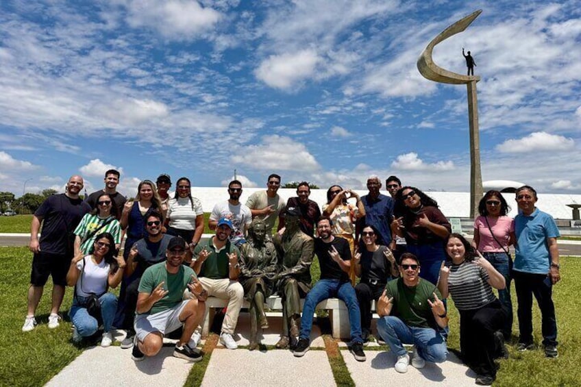 A group of people posing in front of a sculpture and a building. 4