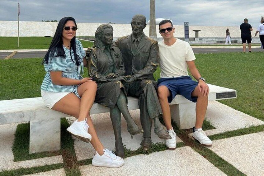 Trois personnes sont assises sur un banc, avec une statue placée entre elles. 3
