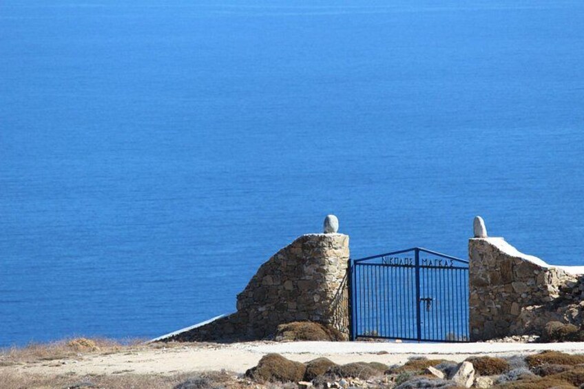 Un muro de piedra con una verja azul y un mar azul transparente al fondo. 2