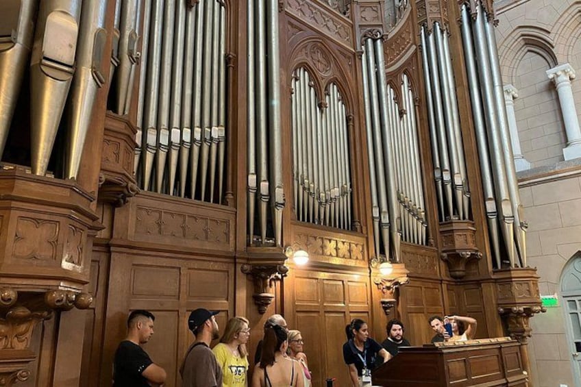 A large pipe organ with multiple rows of pipes, ornate wood carvings, and a group of people standing in front of it. 4