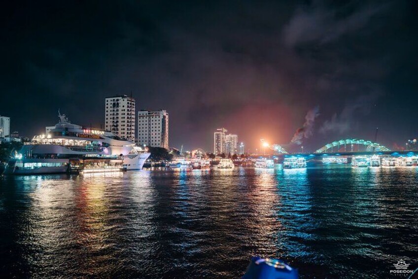 A nighttime cityscape with illuminated buildings, a bridge, and a body of water reflecting lights. 3