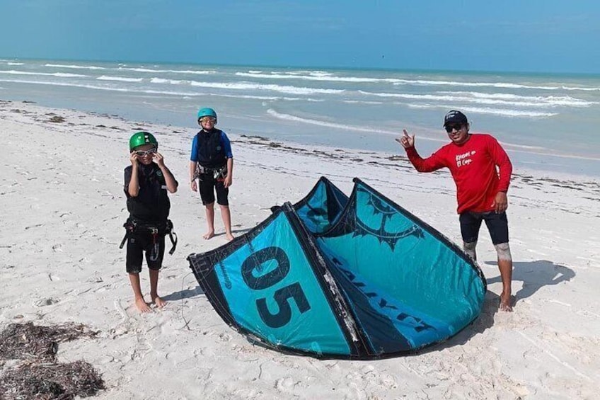 Une plage avec un cerf-volant bleu, une personne portant un t-shirt rouge et deux autres personnes portant des casques. 2