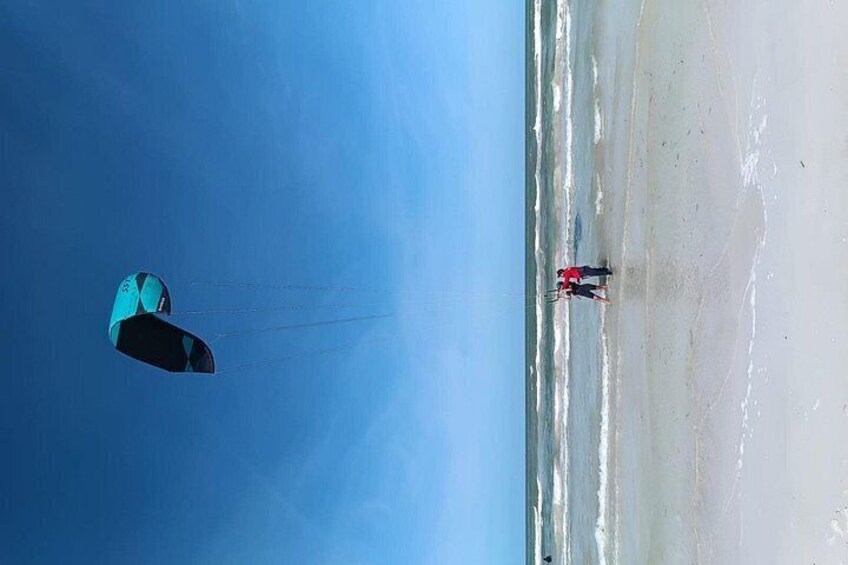 Un pratiquant de kitesurf sur une plage, sous un ciel bleu dégagé. 3