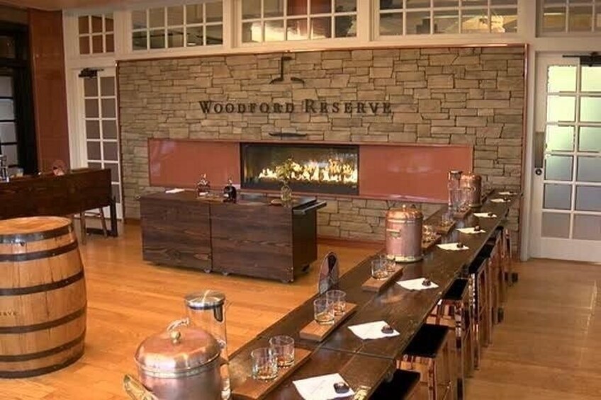 A long wooden bar with copper mugs, a stone fireplace, and a sign reading 'Woodford Reserve.' 2