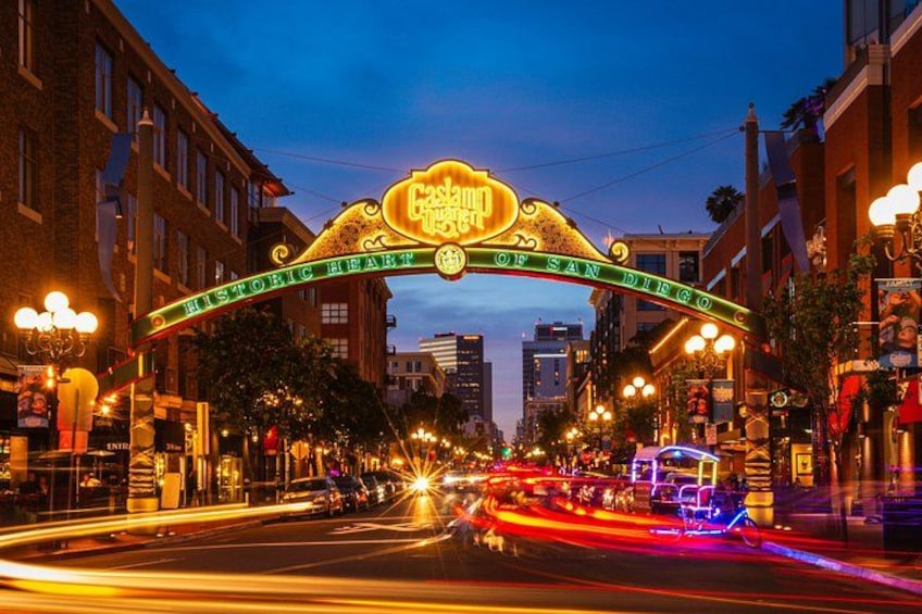 Escena urbana con un letrero de neón que dice 'Casino City of San Diego Historic Heart' y una calle concurrida con estelas de luz. 1