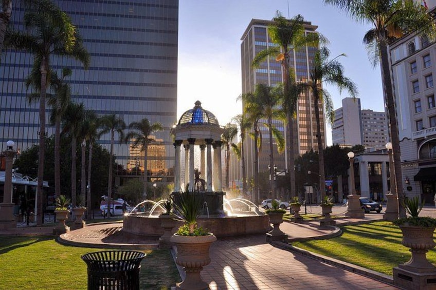 Una plaza urbana con una fuente, palmeras y edificios modernos. 5