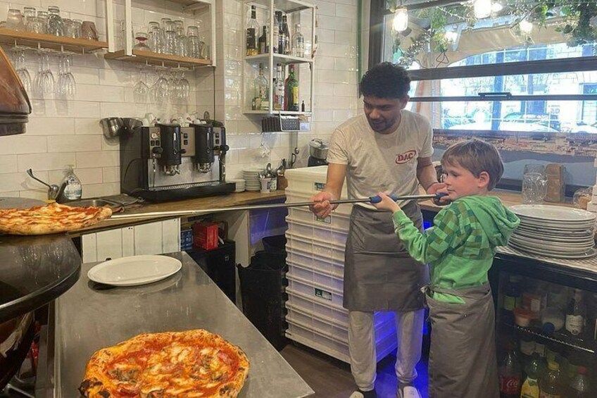 Et køkken med en pizzaovn, en mand og et barn, samt hylder med flasker og glas. 2