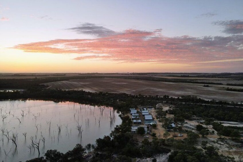 A sunset over a rural landscape with a water body, trees, and scattered buildings. 1