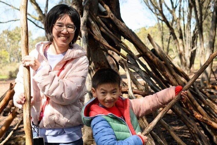 Two people standing near a pile of logs in a wooded area. 5