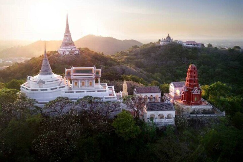 A temple complex with a prominent white pagoda, a red stupa, and a white building on a hilltop. 1