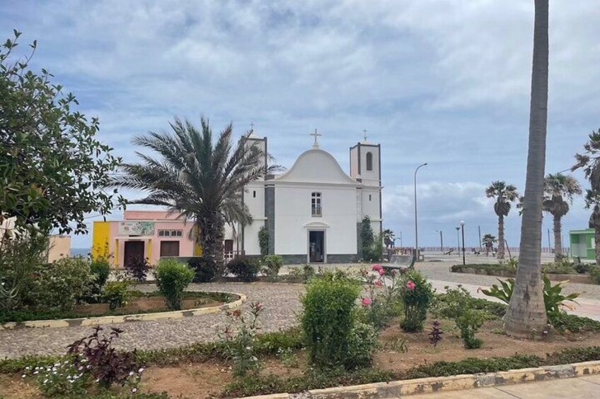 A church with a bell tower, surrounded by palm trees and a garden with flowers. 2