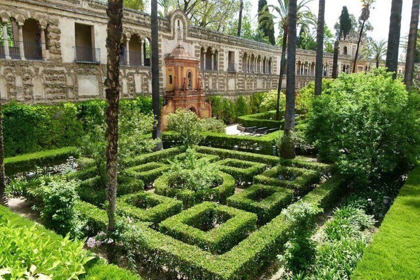 Un jardín formal con setos geométricos, palmeras y arquitectura histórica. 3
