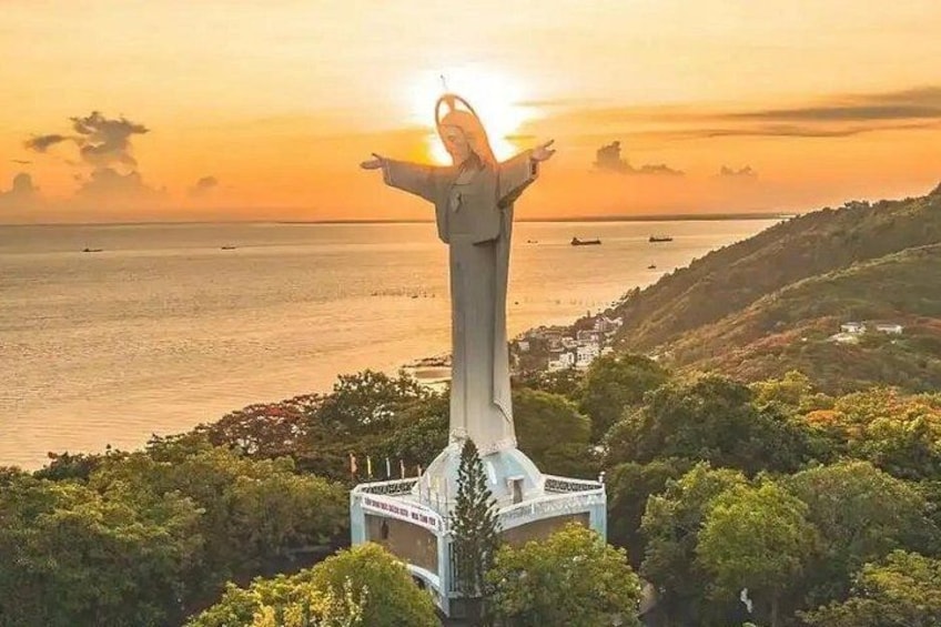 Una estatua con los brazos extendidos, un paisaje costero y una puesta de sol. 2