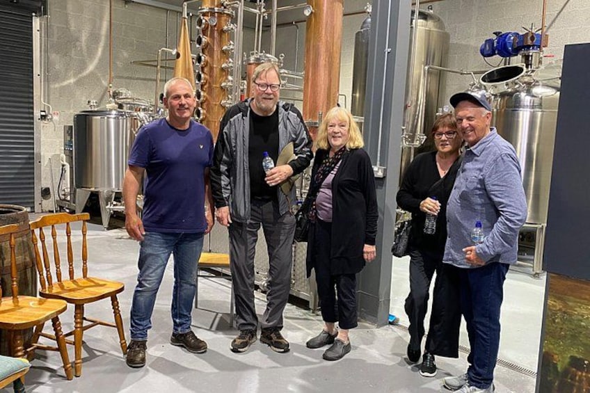 A group of people in a brewery setting with stainless steel tanks and wooden barrels. 5