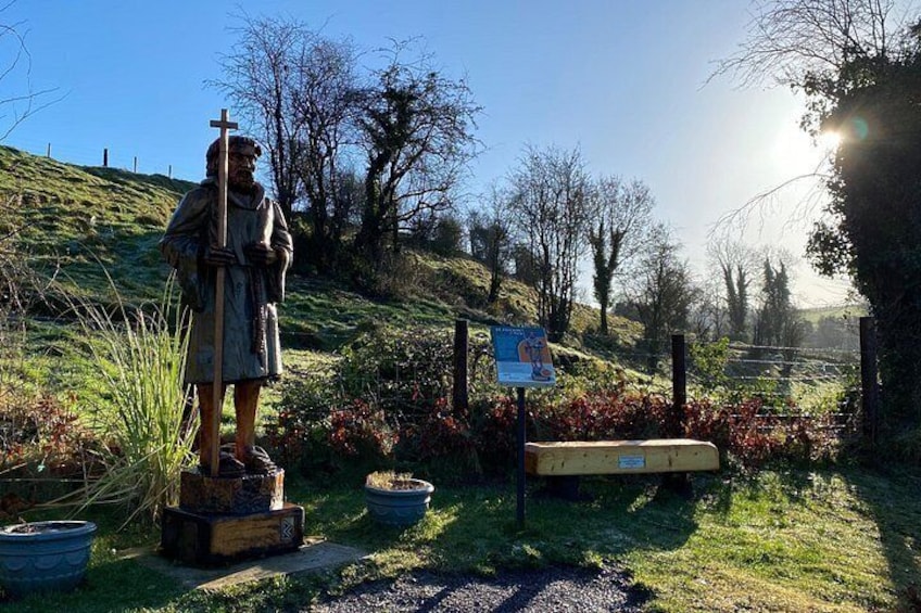Une statue représentant une personne tenant une croix, entourée de verdure et se dressant sous un ciel dégagé. 4