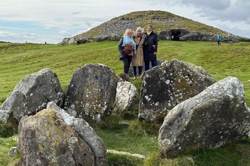 A group of people standing among large rocks in a grassy field with a hill in the background. 1