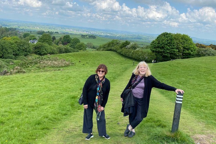 Two people standing on a grassy hill with a view of a landscape in the background. 4