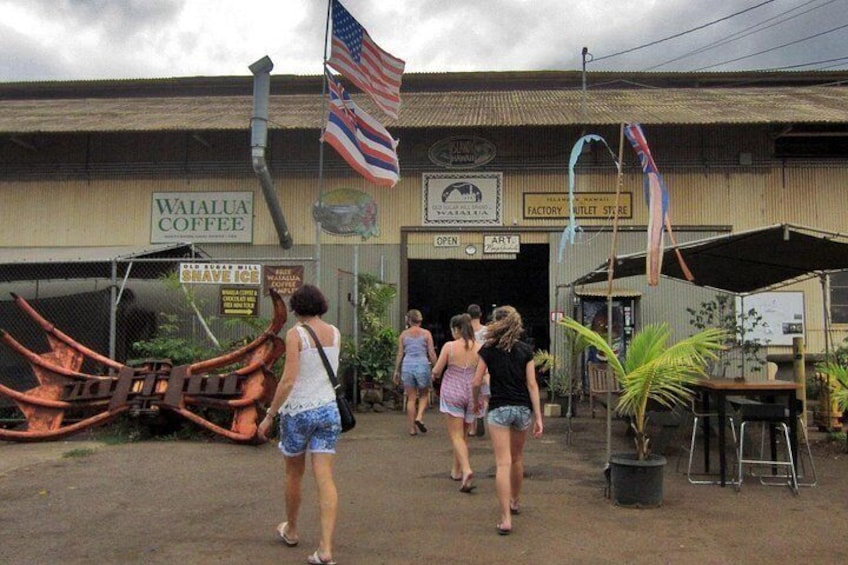 En bygning med skilte for 'Waialua Coffee' og 'Factory Outlet Store'. Folk går foran. 4