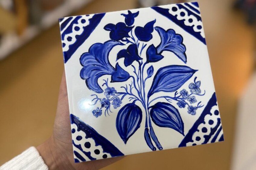 A hand holding a ceramic tile with a blue floral pattern. 4