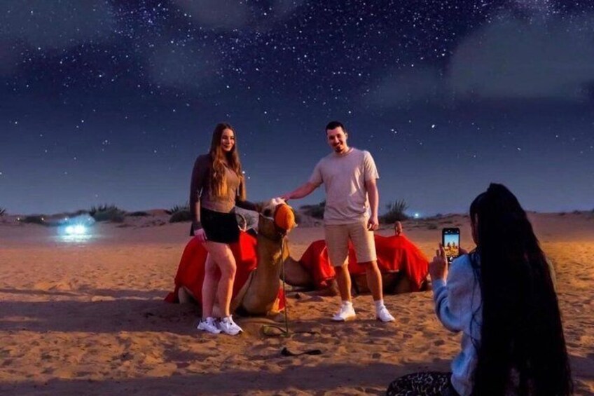 Paesaggio desertico notturno con cielo sereno, stelle visibili e una persona in groppa a un cammello. 1
