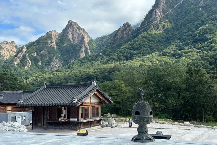 A traditional Korean building with a tiled roof, a stone statue, and a mountainous backdrop. 2