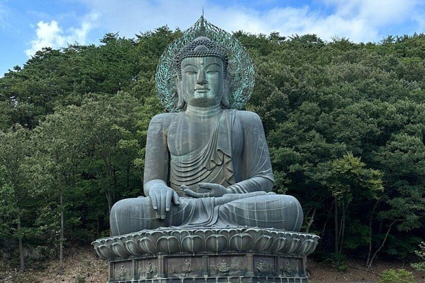 A large seated Buddha statue surrounded by lush greenery. 3