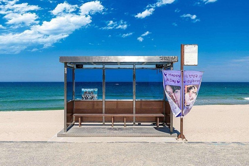 A beachside bus stop with a clear view of the ocean and a signboard. 1