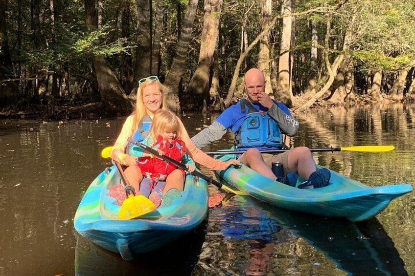 Two people kayaking on a calm river surrounded by trees. 3