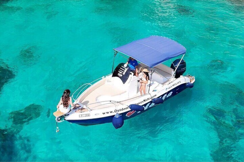 A boat with a blue canopy and a website URL on its side, floating on clear turquoise water. 5