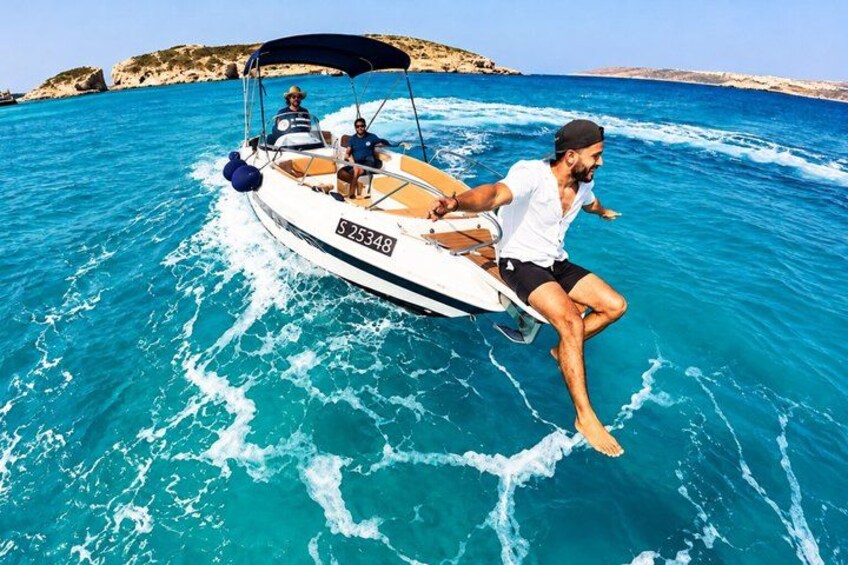 A boat with two people on the water, a rocky coastline in the background, and clear blue water. 1