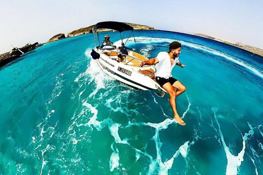 Iemand rijdt op een jetski over turquoise water, met een boot op de achtergrond en een rotsachtige kustlijn. 2