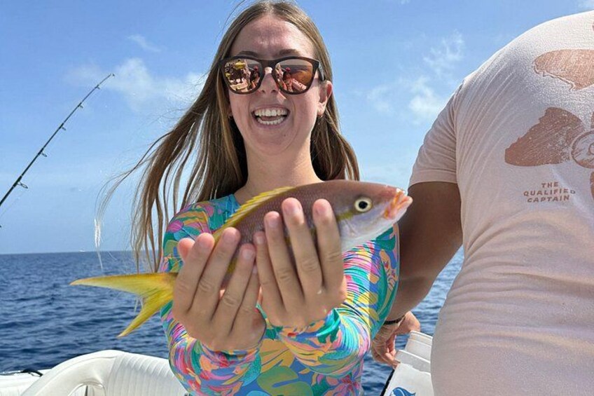 En person håller i en fisk på en båt med havet i bakgrunden. 4
