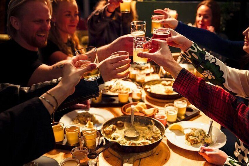 A group of people toasting with drinks around a table with food. 1