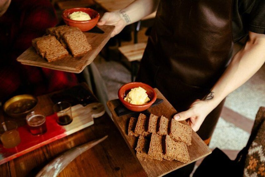 A person serving slices of bread on a wooden board with a bowl of butter. 3