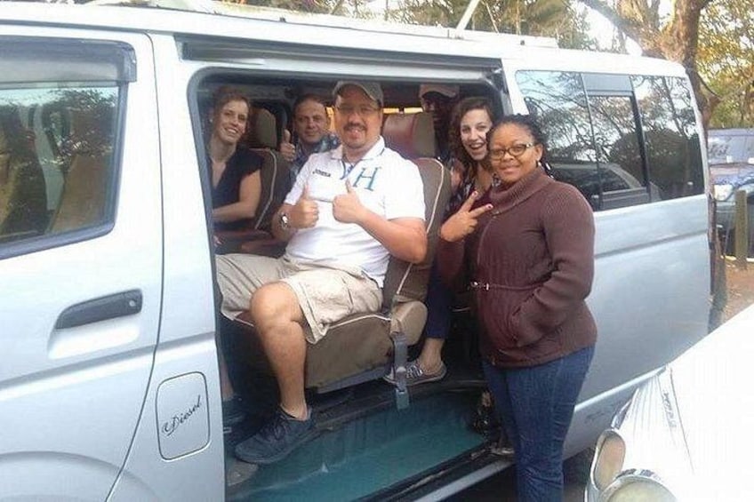 A white van with its door open, a person sitting inside, and three people standing outside. 1