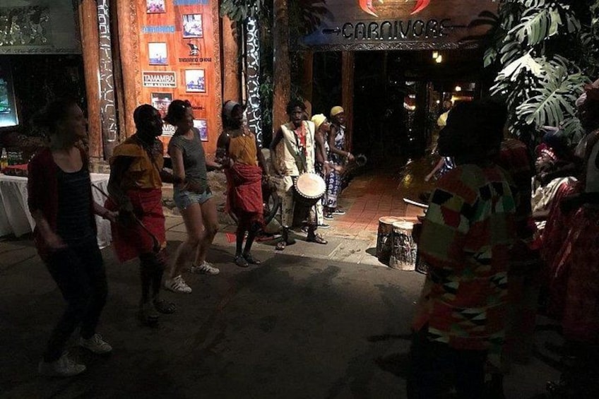 A group of people dancing in an outdoor setting with a sign that reads 'CARNAVAL.' 4