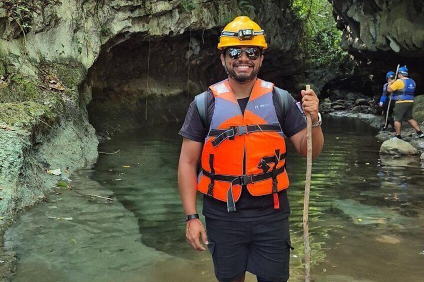Eine Person in einer Höhle mit einem Wasserlauf, trägt eine Schwimmweste und einen Helm. 1