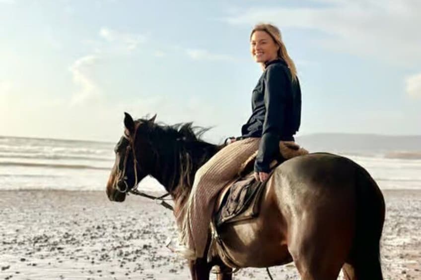 A person riding a horse on a beach with the ocean in the background. 4