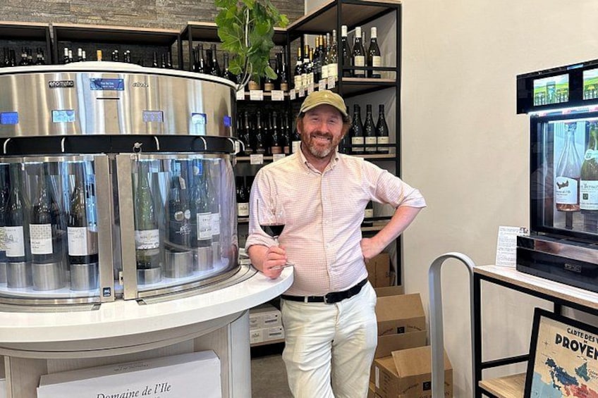 Un homme se tient dans un magasin de vins, entouré de bouteilles et devant un présentoir réfrigéré. 1