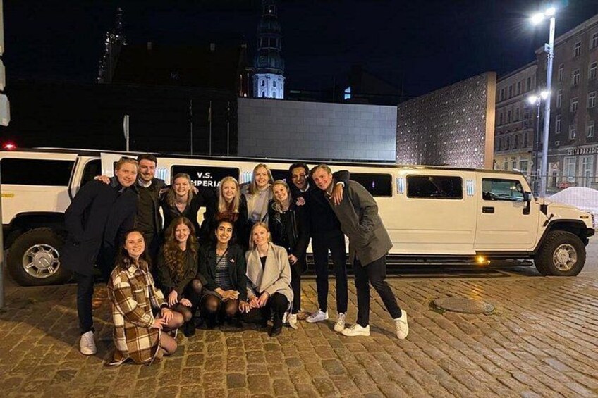 A group of people posing in front of a white vehicle on a cobblestone street at night. 4