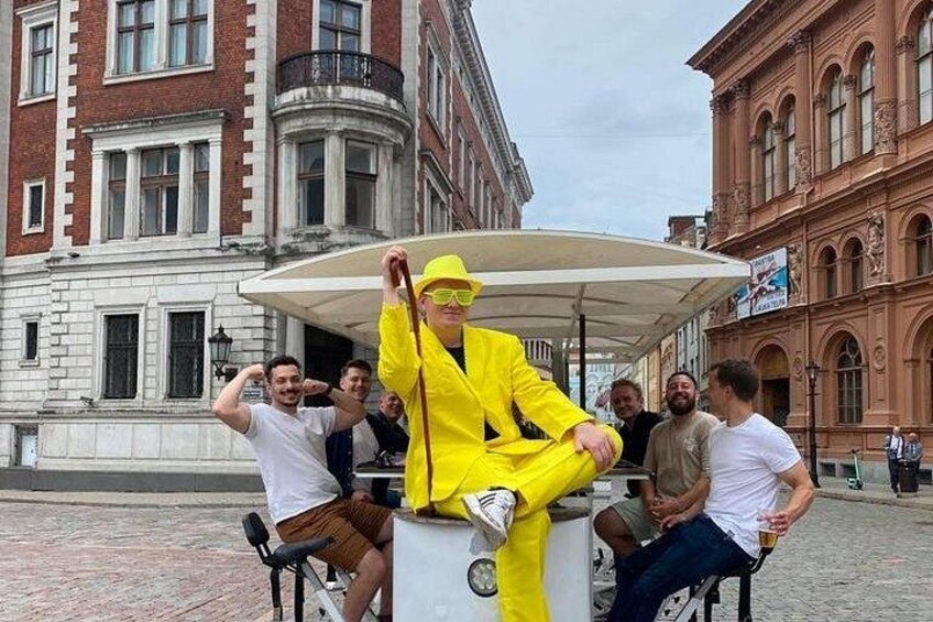 A person in a yellow suit sitting on a bench with a group of people around. 2