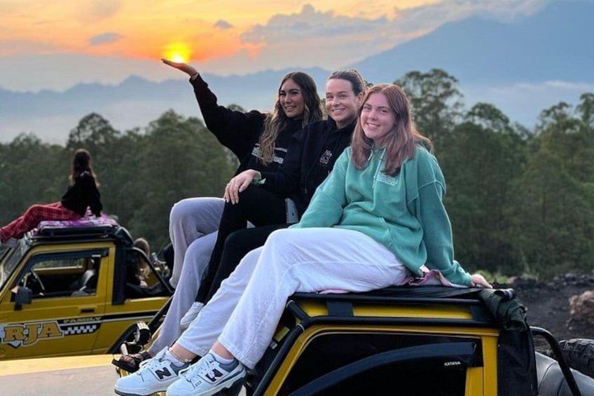 Three people sitting on a yellow vehicle with a sunset in the background. 2