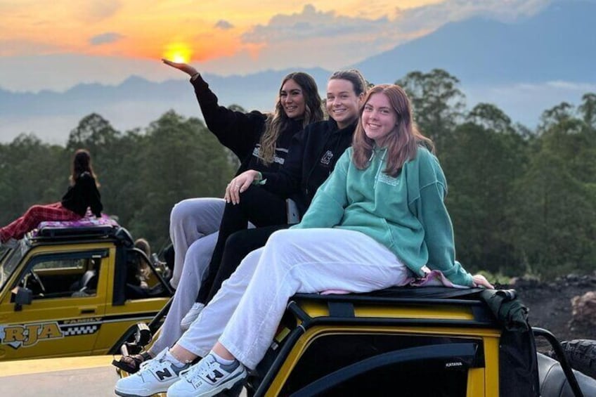 Three people sitting on a yellow vehicle with a sunset in the background. 2