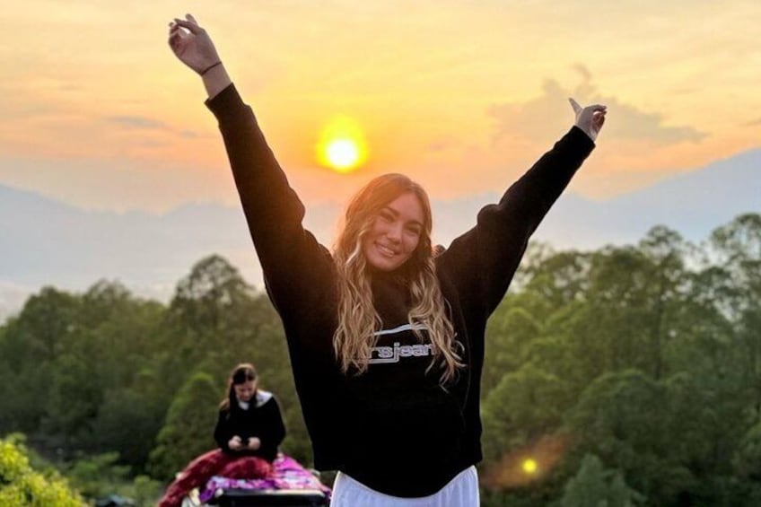 A person with arms raised against a sunset, wearing a black hoodie with 'Bjean' text, and a forested landscape in the background. 3