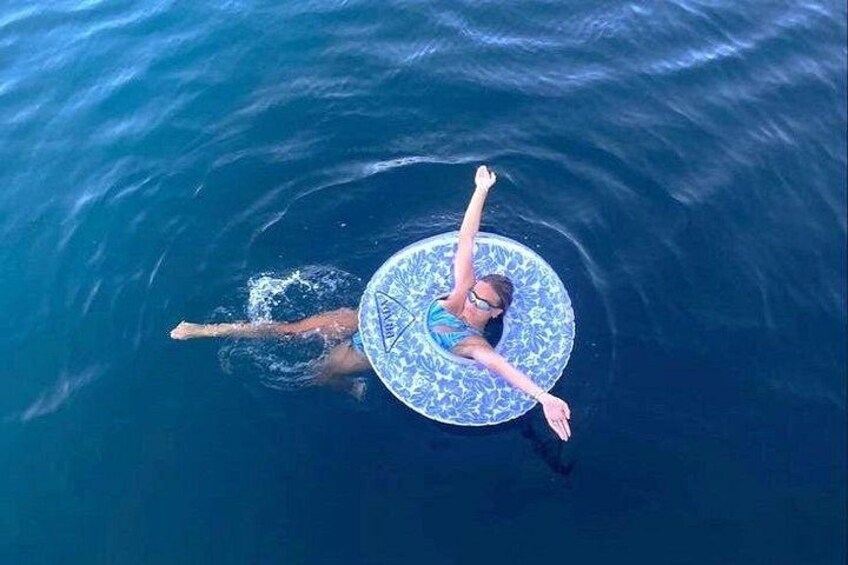 A person floating on a blue and white patterned circular object in the ocean. 5