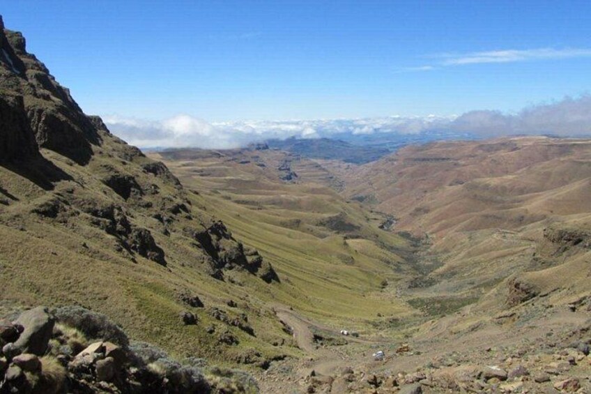 A mountainous landscape with a valley, rocky terrain, and distant snow-capped mountains. 2